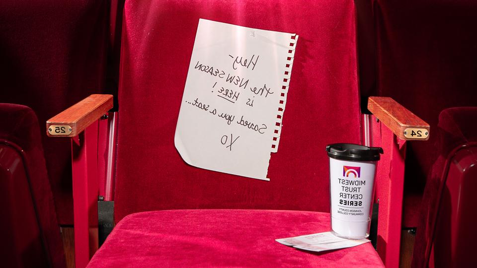 a velvet theatre chair in Yardley Hall with a note on it that reads Hey - the new season is here! Saved you a seat... xo